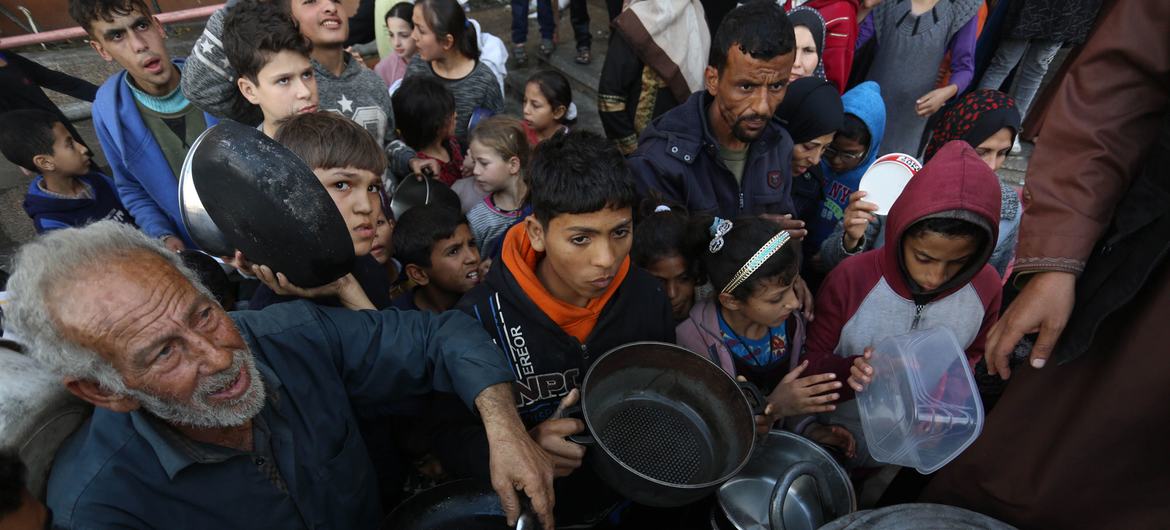 Palestinos deslocados esperam para coletar alimentos em um ponto de distribuição próximo a uma escola que virou abrigo