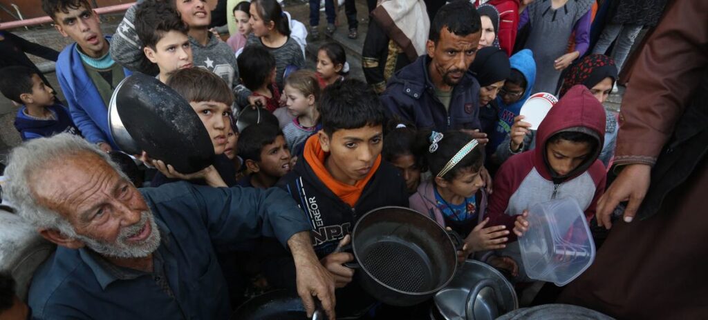 Palestinos deslocados esperam para coletar alimentos em um ponto de distribuição perto de uma escola que virou abrigo em Gaza