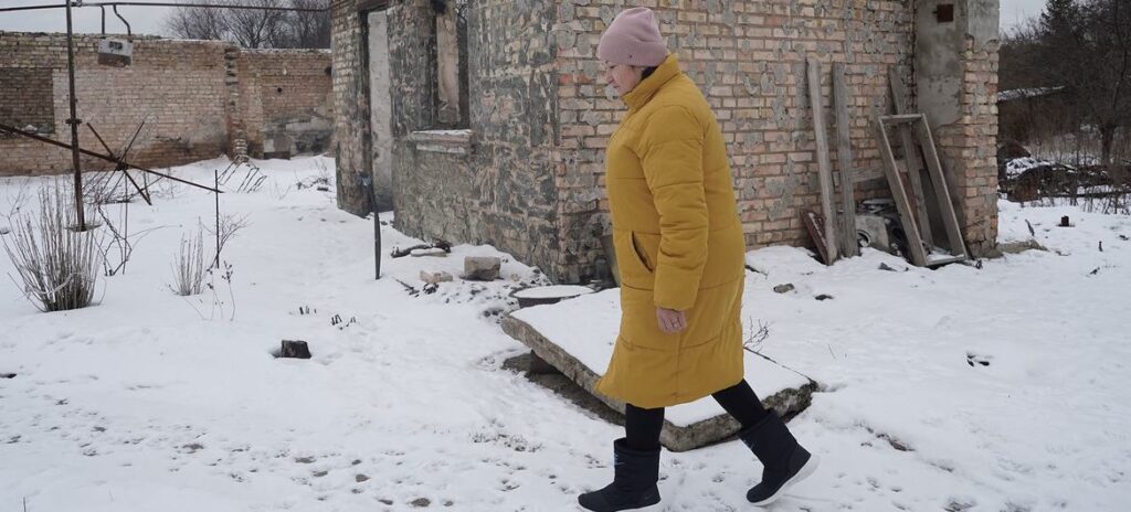 Uma mulher passa por sua casa danificada na vila de Horenka, no Oblast de Kiev