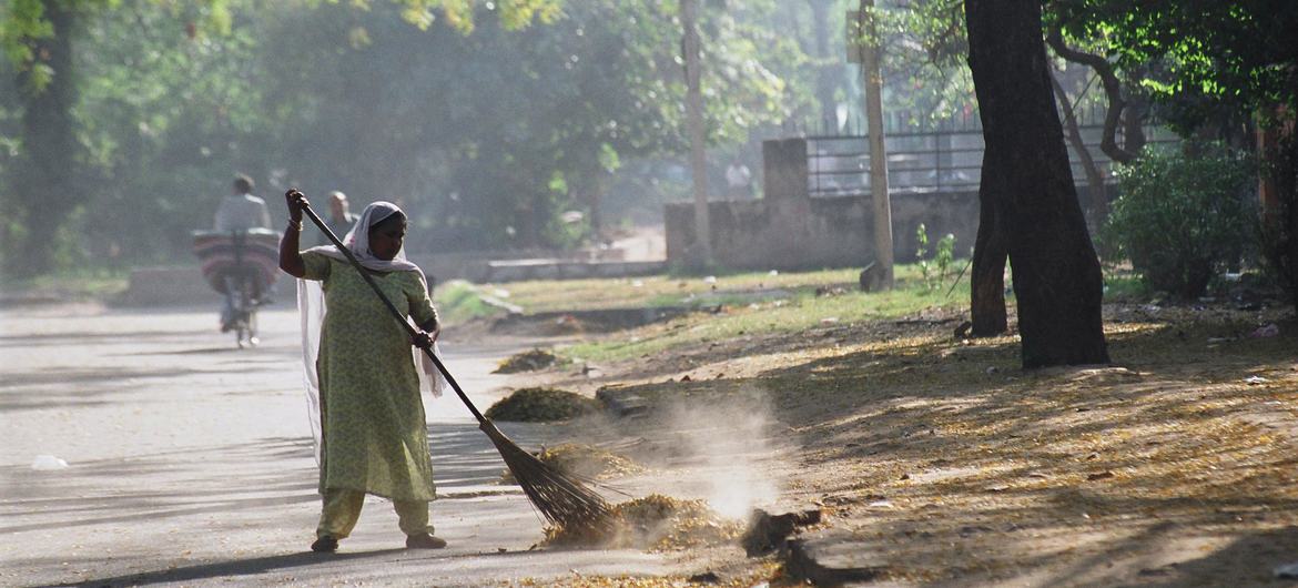 Uma trabalhadora doméstica varre a rua em um bairro nobre de Delhi, Índia