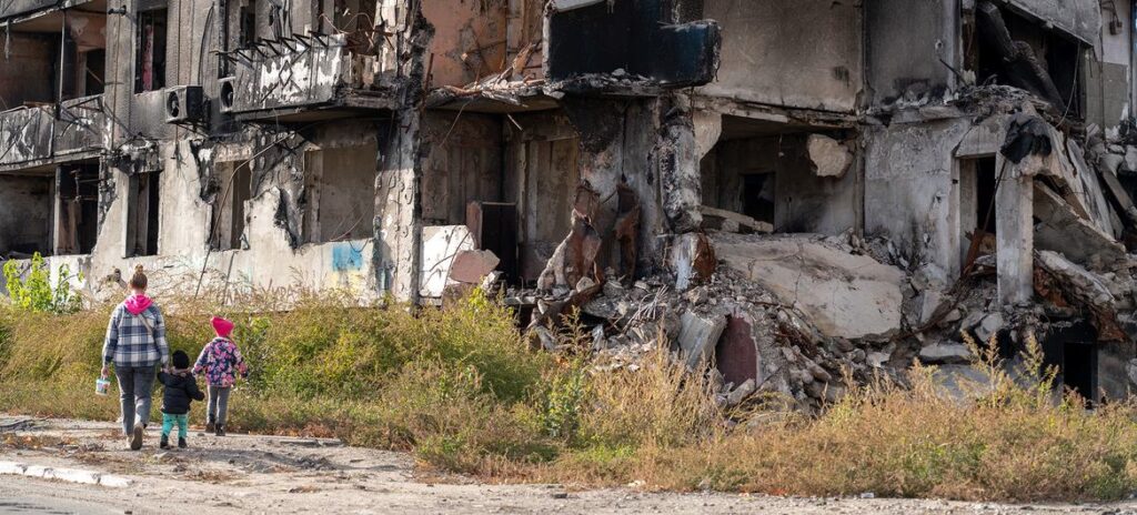 Um adulto e duas crianças passam por um prédio destruído em Borodianka, Ucrânia