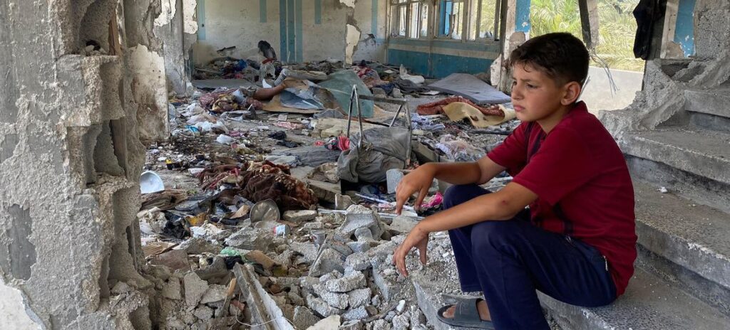 Criança sentada entre as ruínas de uma escola no centro de Gaza