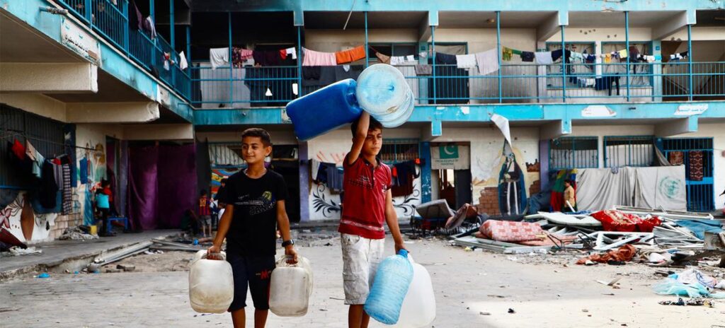 Duas crianças em um abrigo escolar da Unrwa em Khan Younis, no sul de Gaza, indo buscar água.