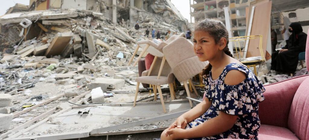 Uma menina senta-se entre os escombros de edifícios destruídos em Gaza.